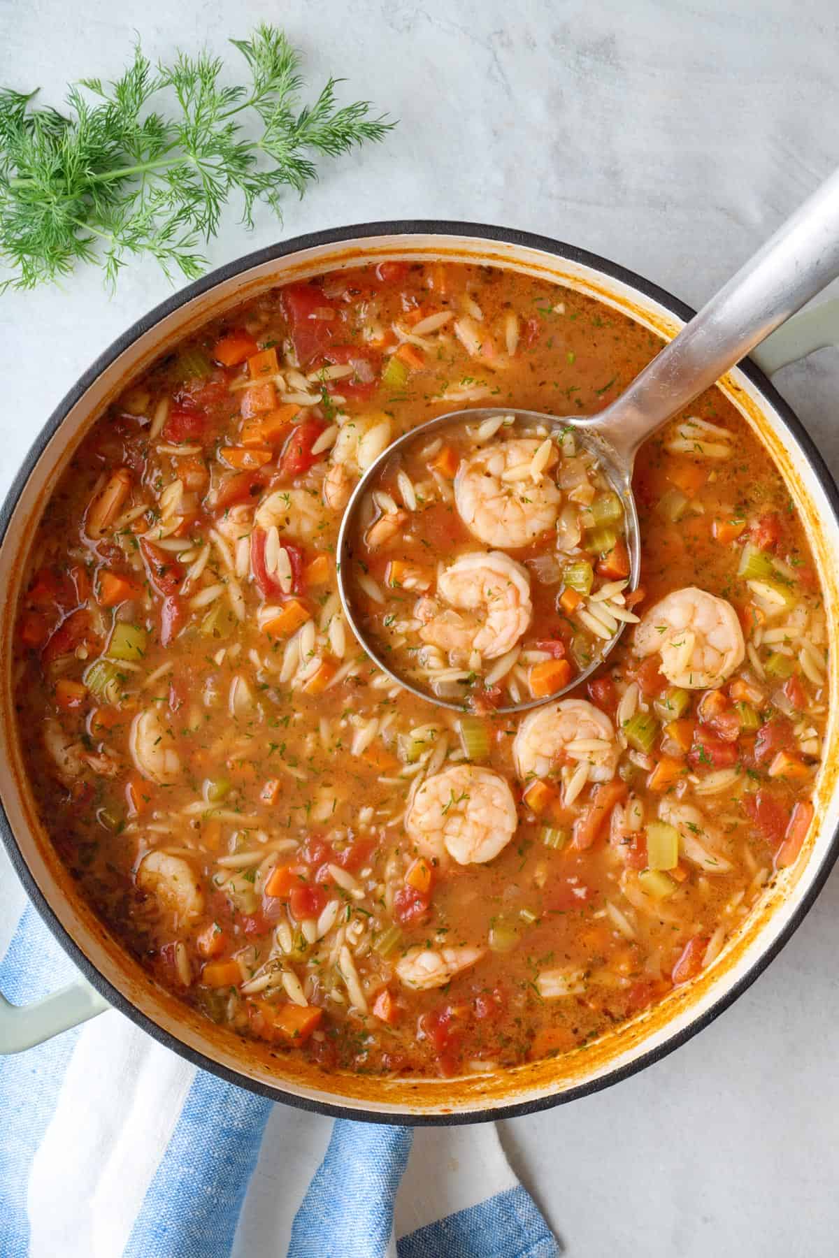 Orzo shrimp soup in a pot with a ladle dipped inside.