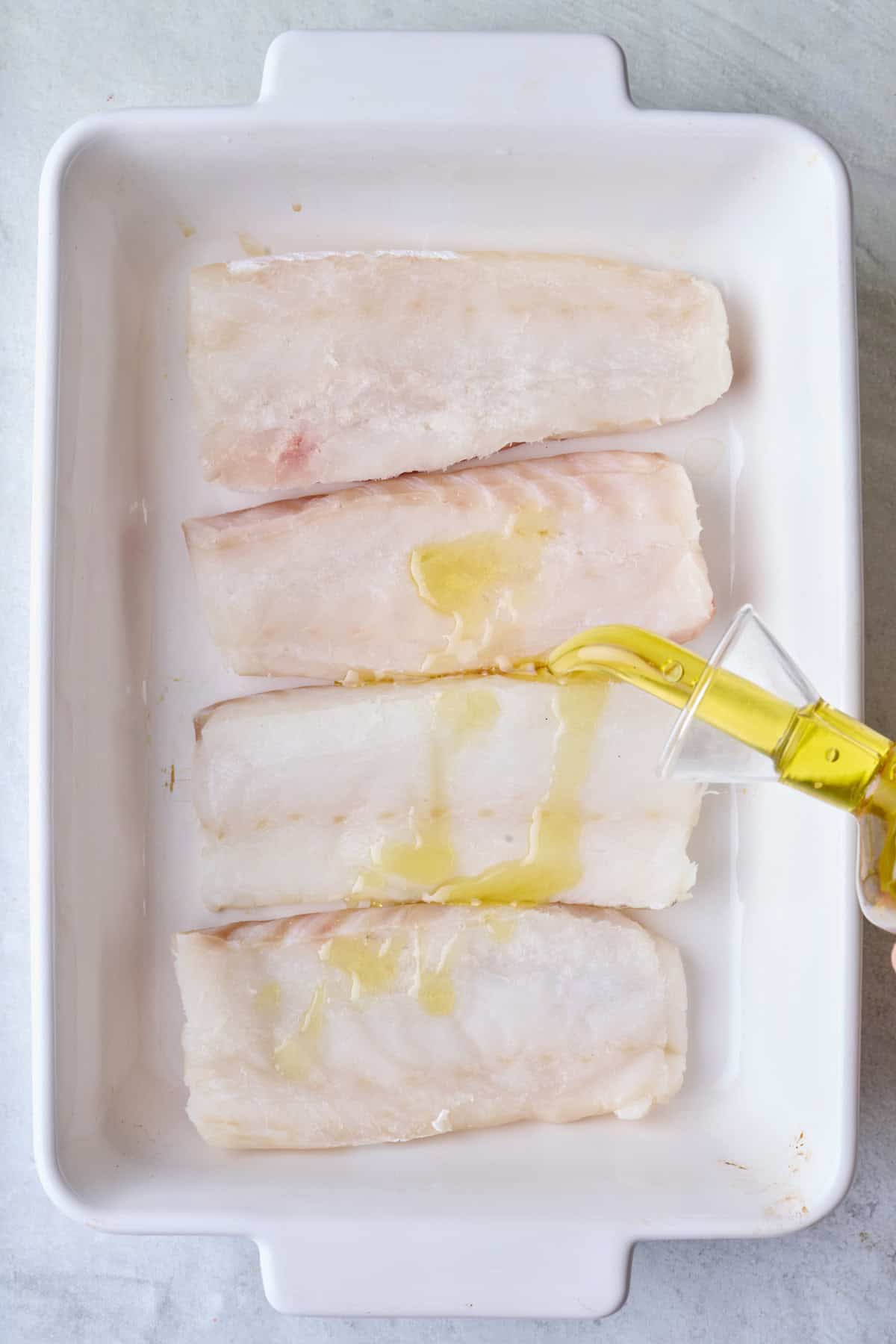 Pouring oil over fish in a baking dish.