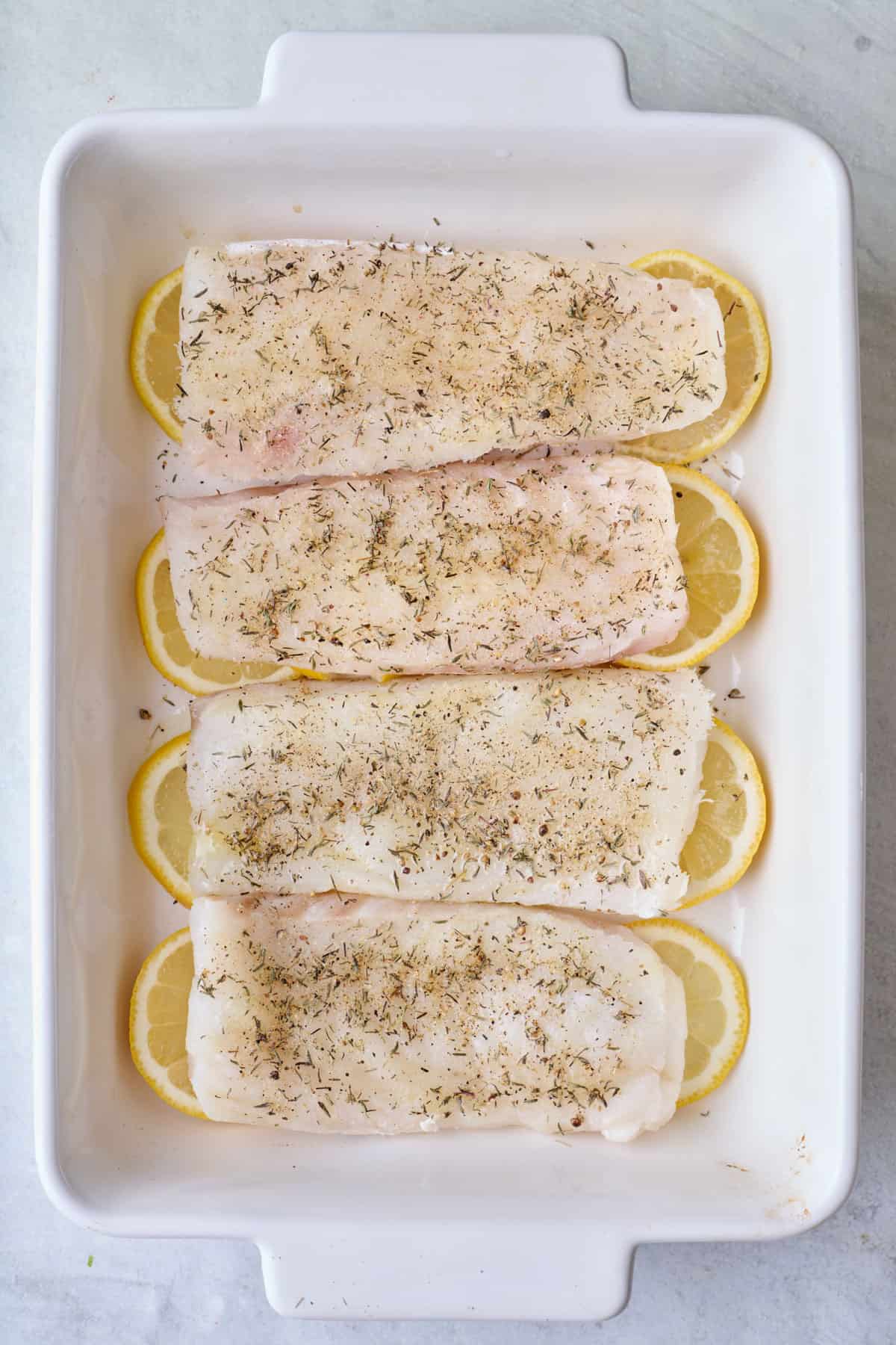 Lemon slices arranged under seasoned fish in baking dish.