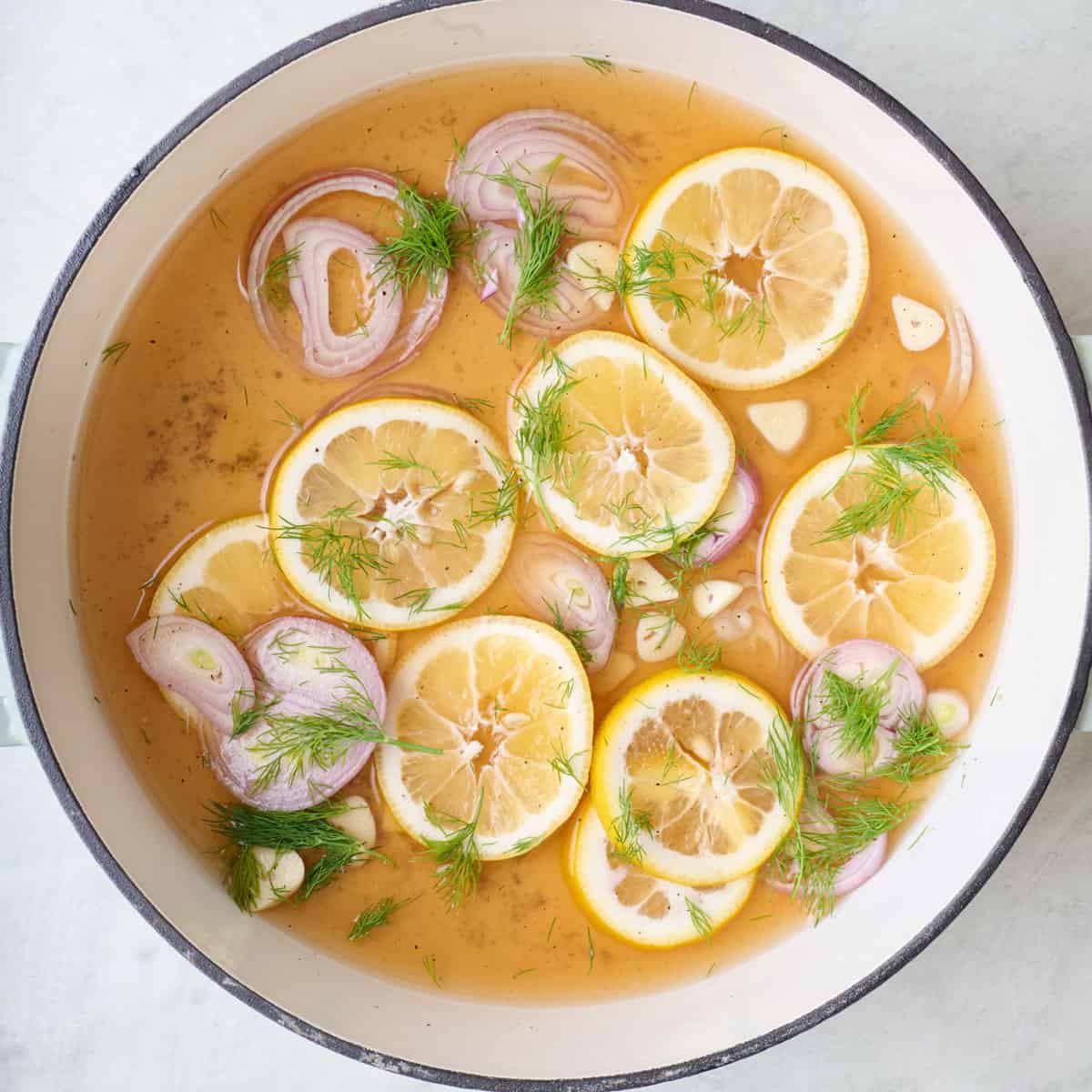 Broth with vinegar, lemon, shallot, garlic, dill, and pepper in a skillet.