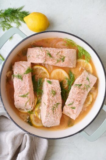 Poached salmon fillets in a pan with lemon slices and fresh dill.