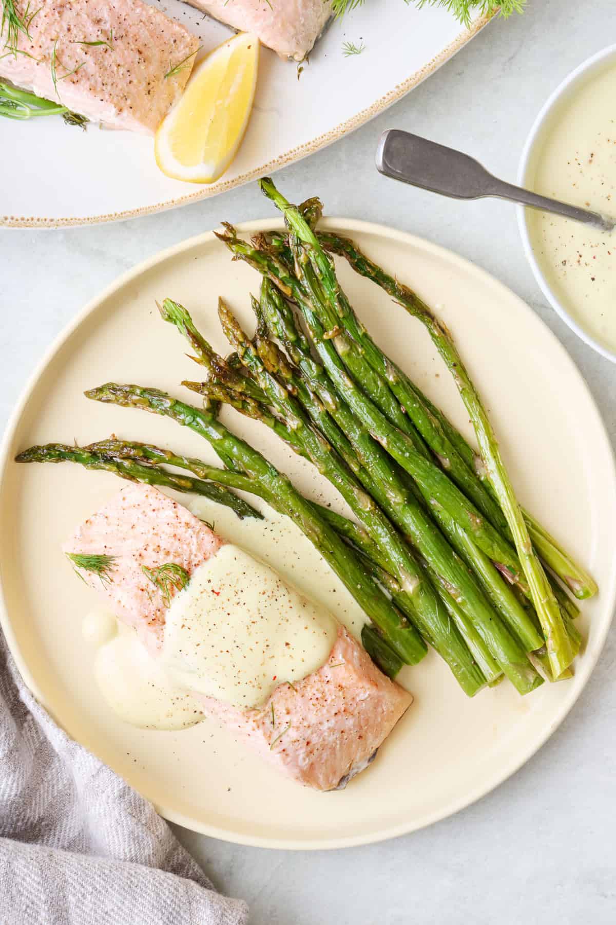 Poached salmon fillet on a plate with asparagus with hollandaise sauce spooned over the salmon.