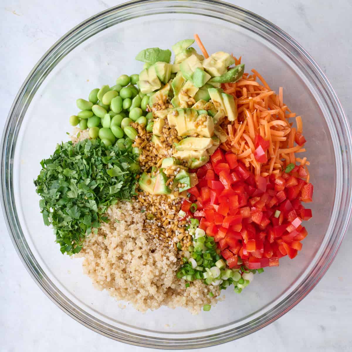 Cooked quinoa, edamame, carrots, pepper, green onion, and cilantro in a large bowl with dressing poured on top.