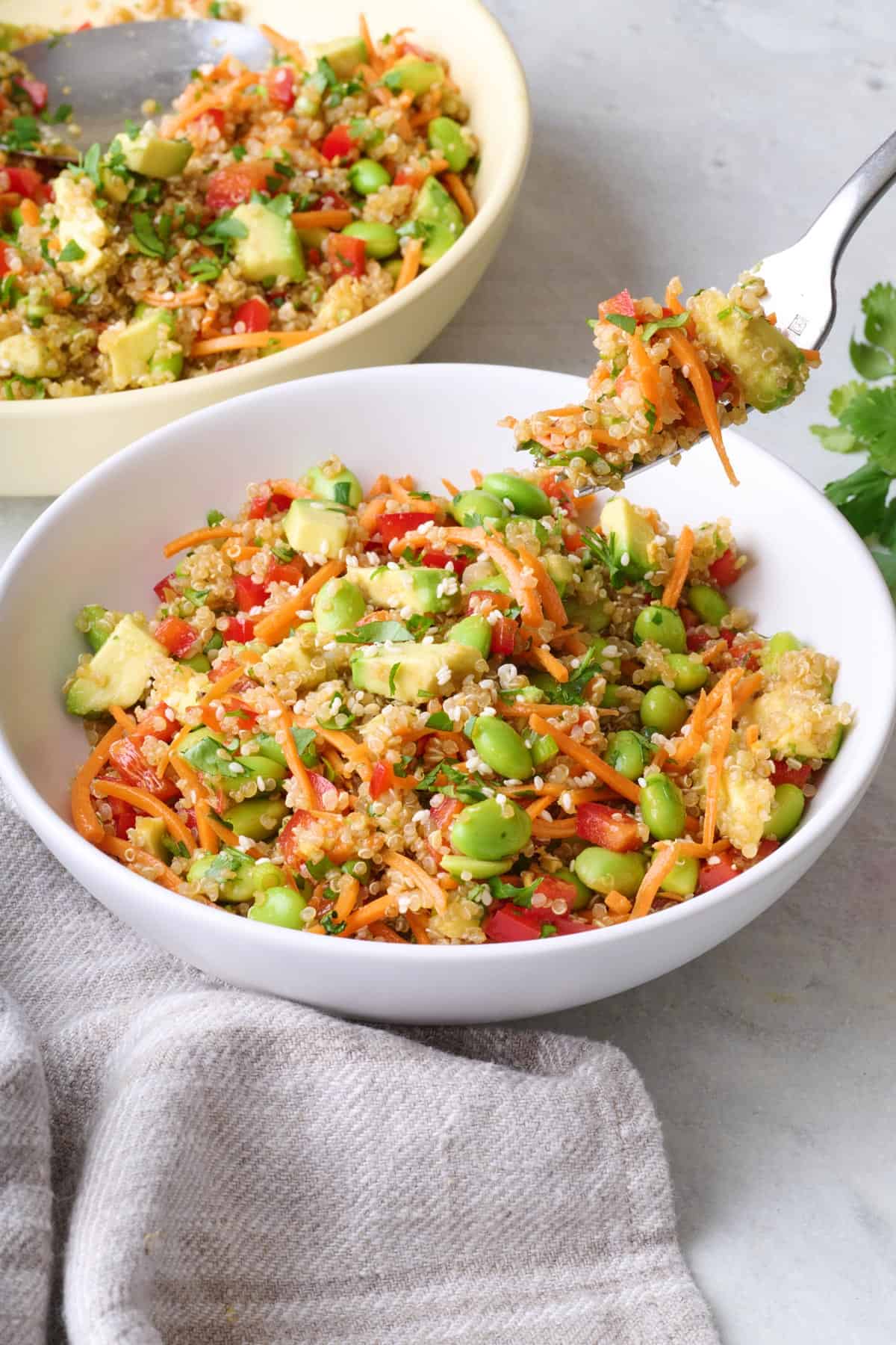 Fork lifting up a bite of quinoa edamame salad from a serving bowl.