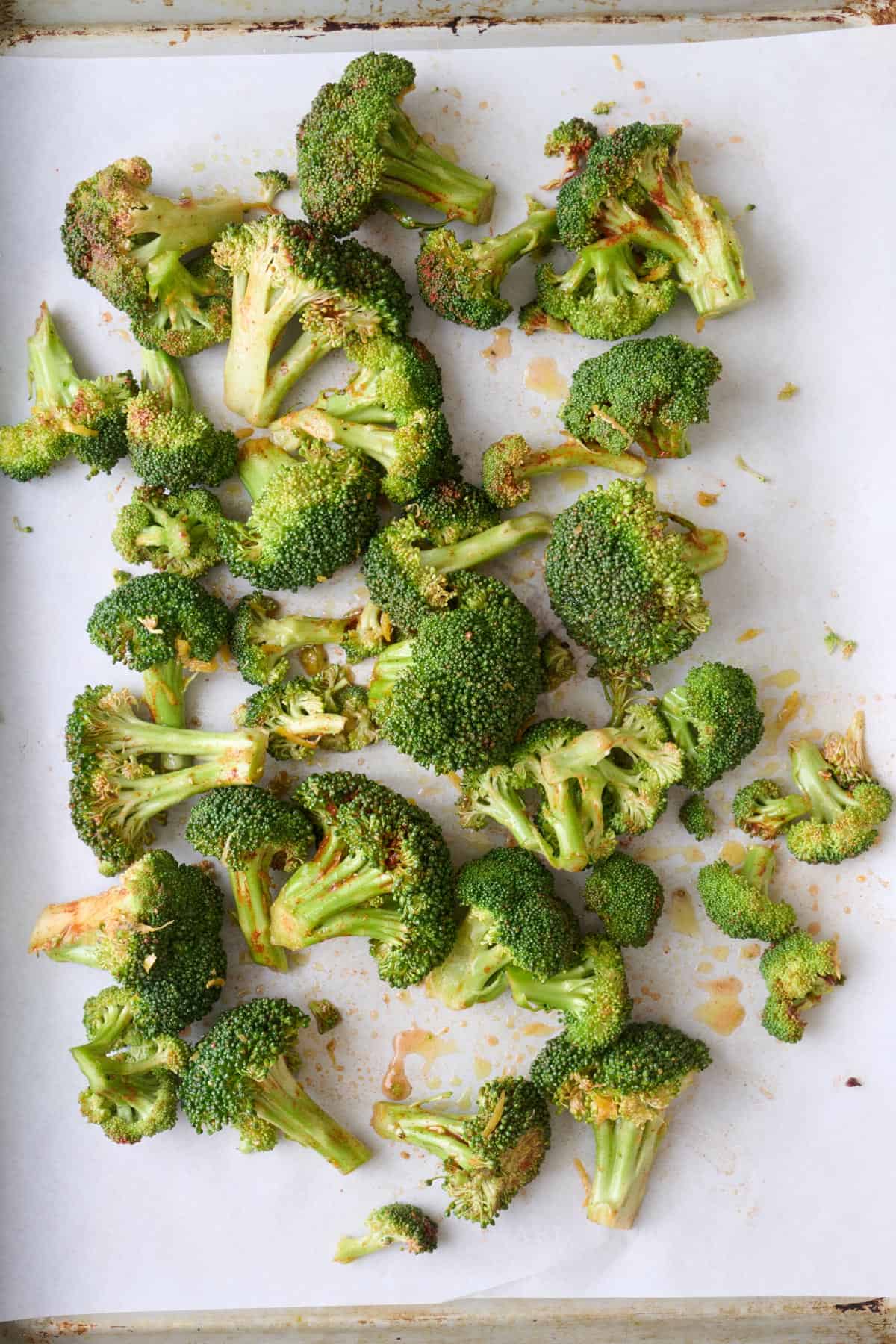 Seasoned broccoli spread onto a parchment lined baking sheet.