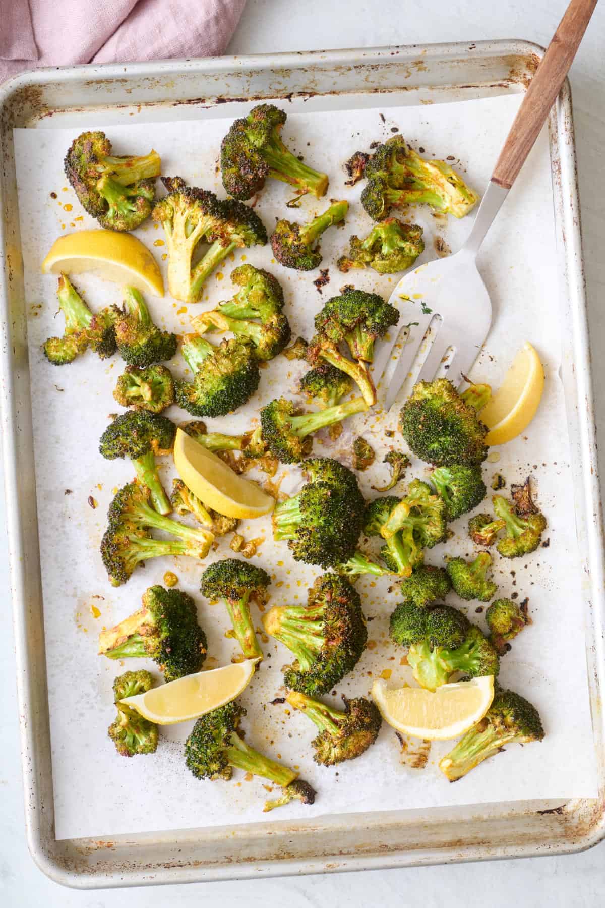 Roasted broccoli on a sheet pan with lemon wedges.