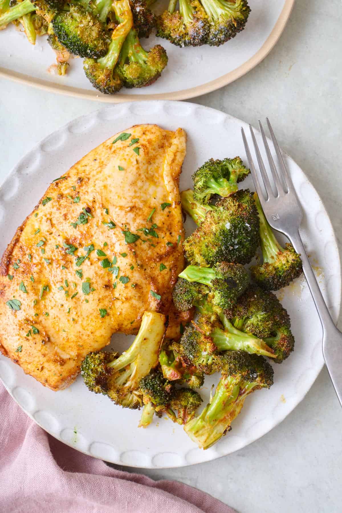 Roasted broccoli on a small plate with chicken.