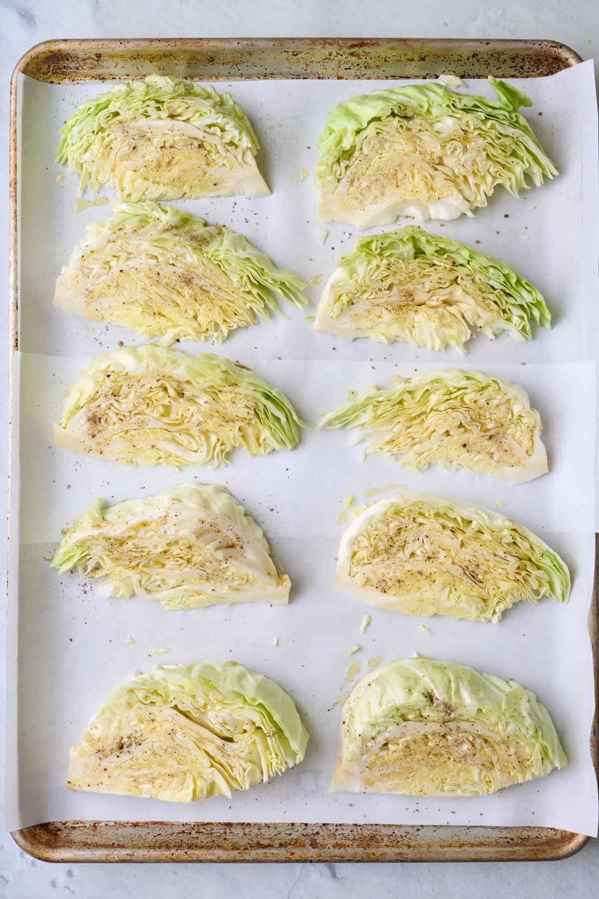 Cabbage wedges on parchment line baking sheet coated with oil and seasoning before cooking.