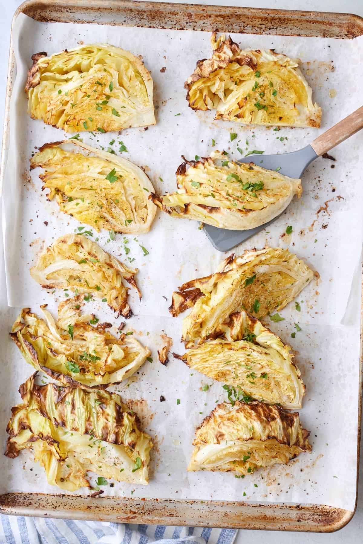 Roasted cabbage wedges on sheet pan slightly angled, with a spatula under one.