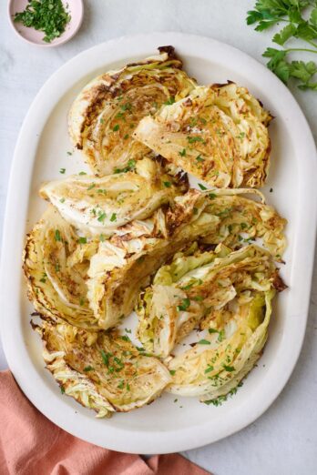 Roasted cabbage wedges on a platter with a serving set resting on plate, garnished with fresh parsley.