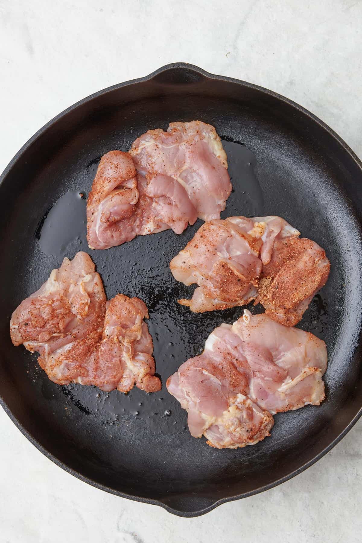 Seasoned chicken thighs in an oiled cast iron skillet before cooking.