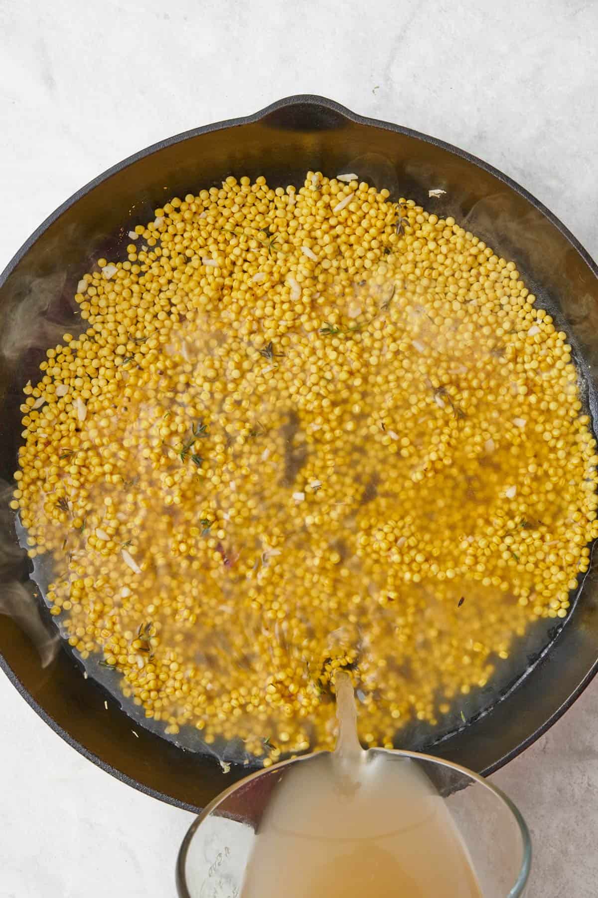 Broth being poured into pan after toasting couscous.