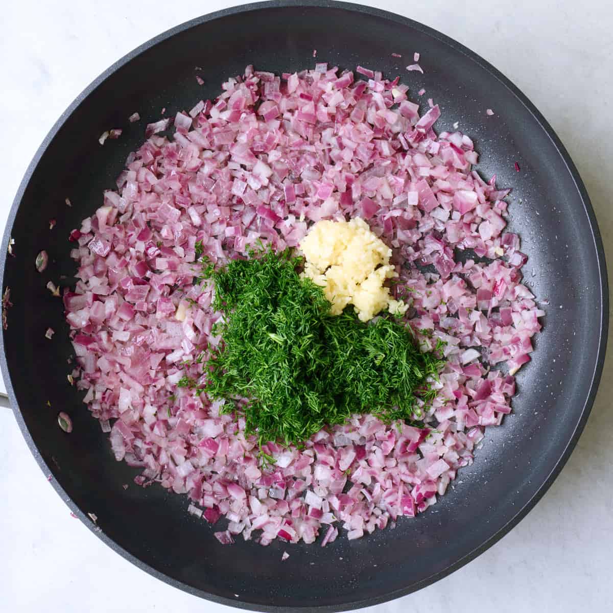 Cooked onions in a skillet with garlic and dill added.