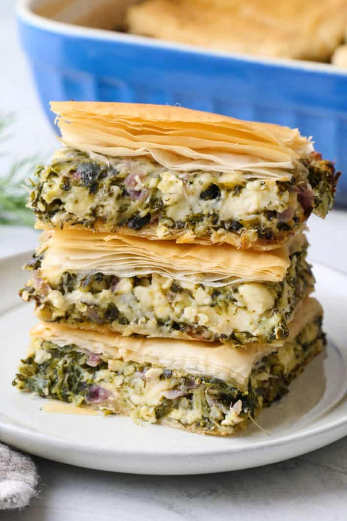 Spanakopita squares stacked on top of each other to show flaky layers and spinach feta filling.