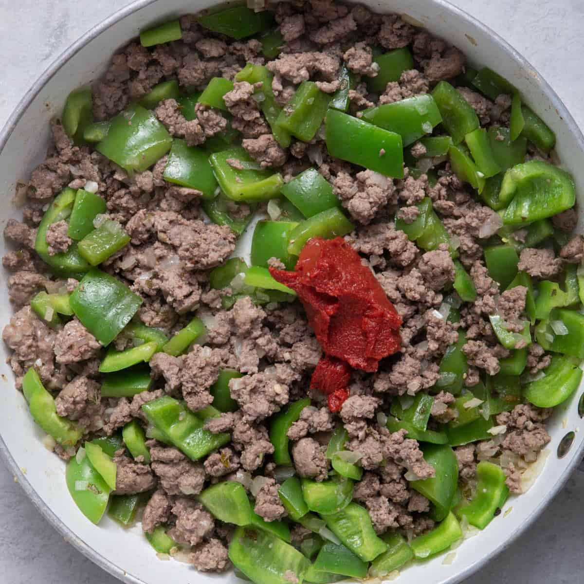 Cooked ground beef mixture with tomato paste on top.