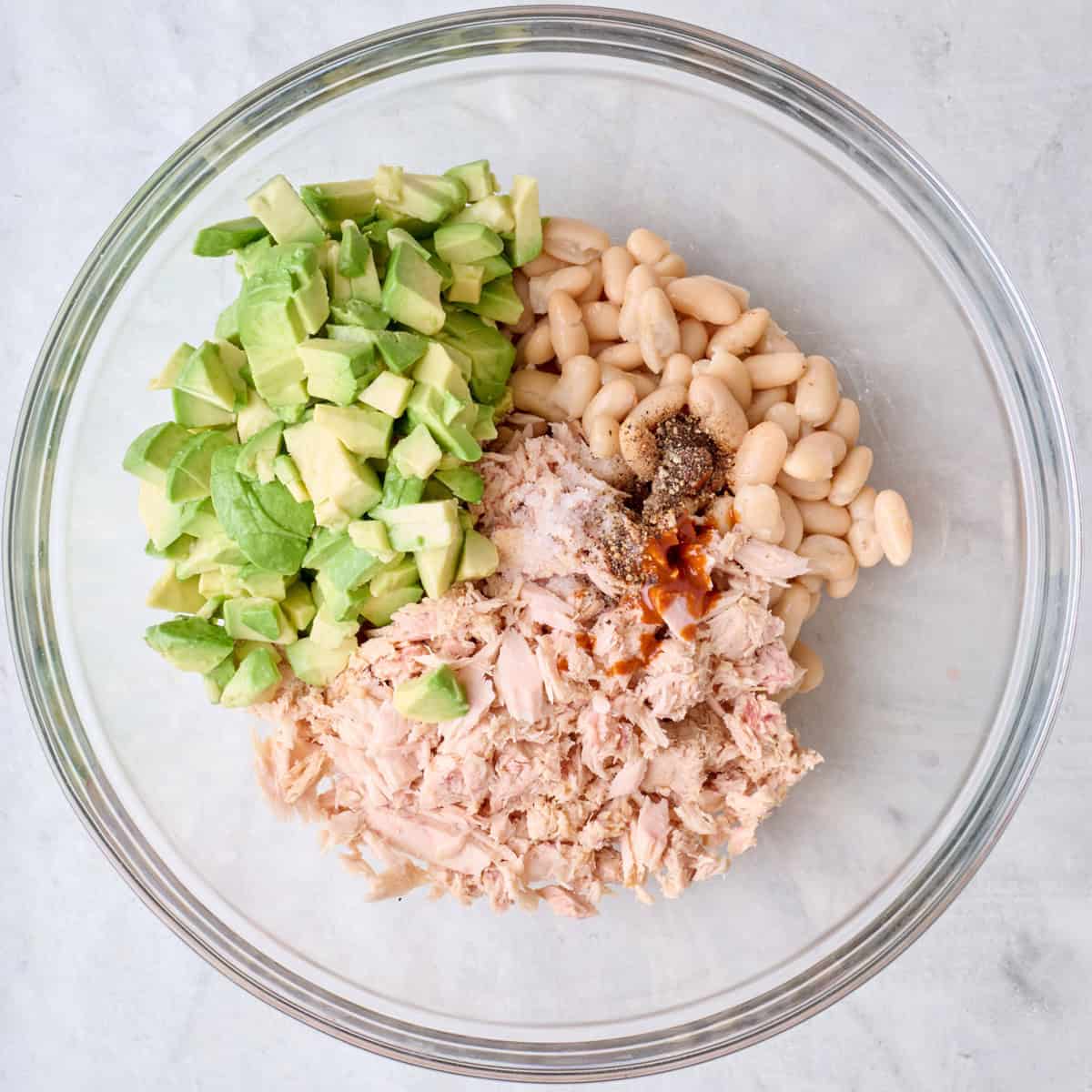 Tuna, diced, avocado, white beans, and seasoning in a bowl.