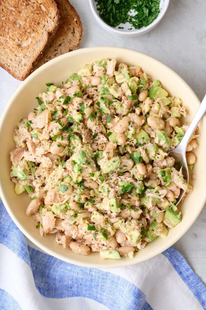 White bean tuna salad in a bowl garnished with fresh parsley with toast slices nearby.