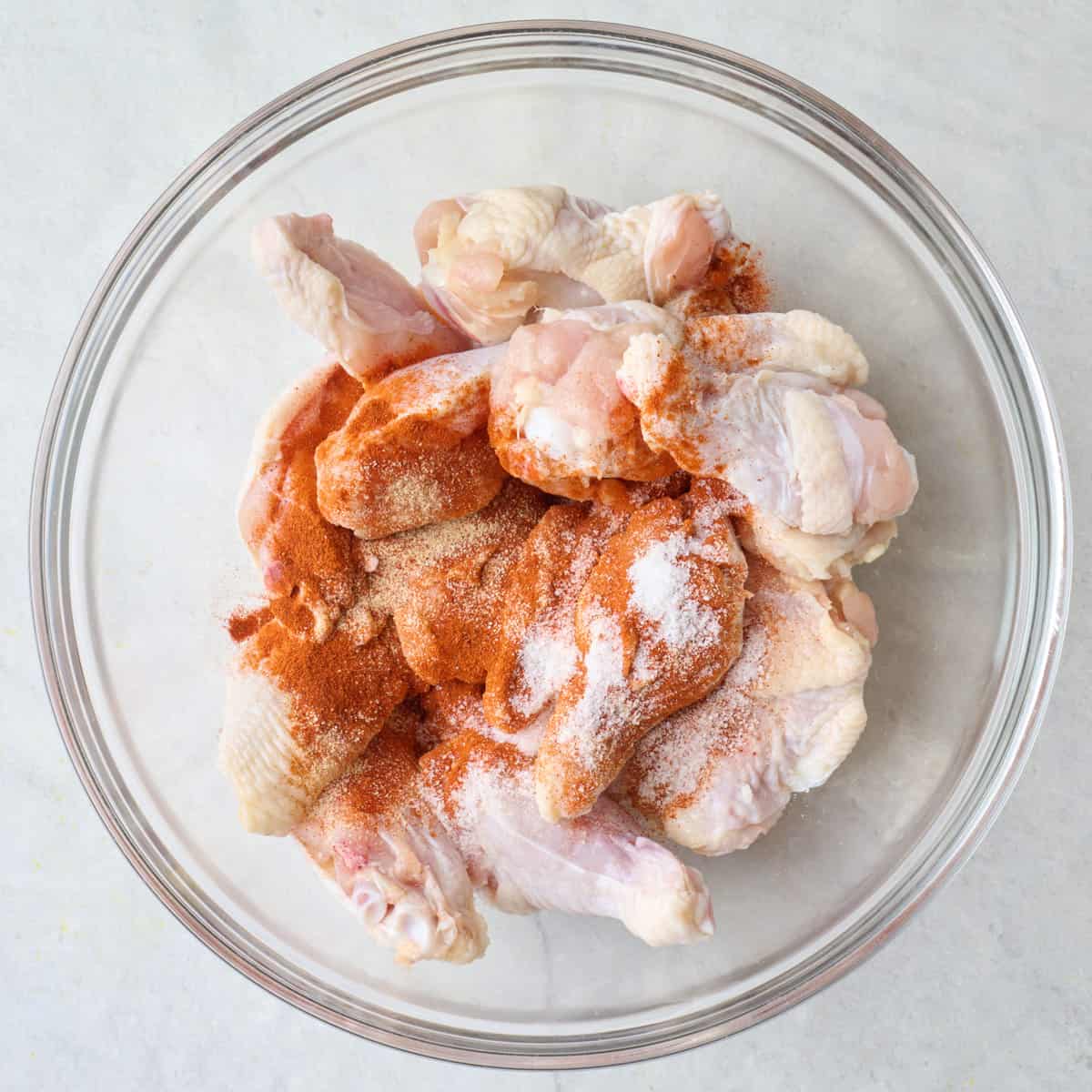 Chicken wings in a bowl with spices before tossing.