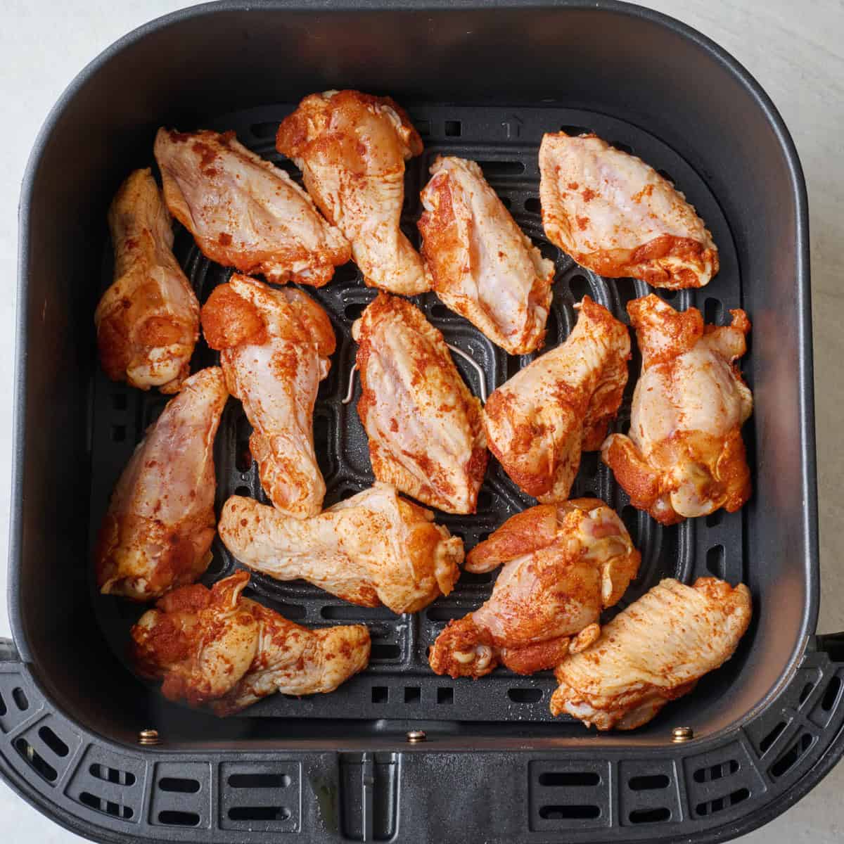 Seasoned chicken wings in an air fryer basket before cooking.