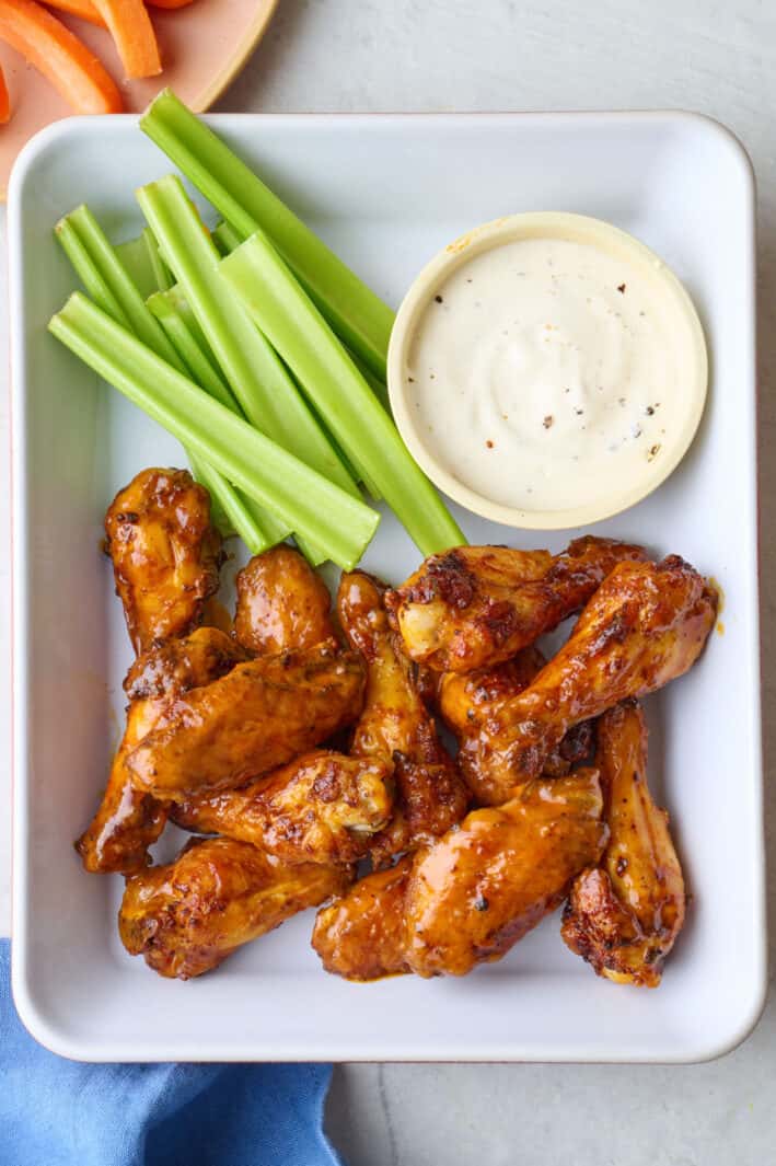 Air fryer buffalo wings on a platter with a side of ranch and celery sticks.