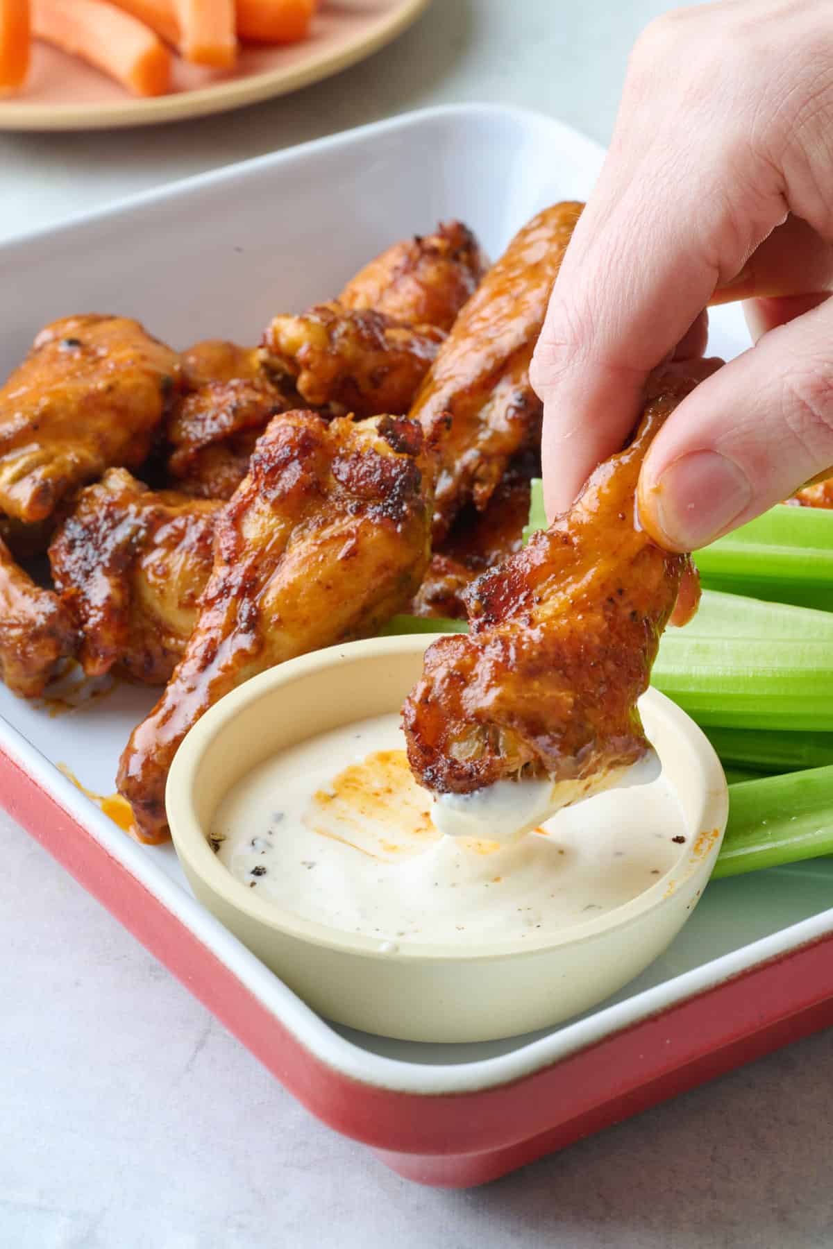 Crispy air fryer chicken wings tossed iin buffalo sauce being dipped into ranch.