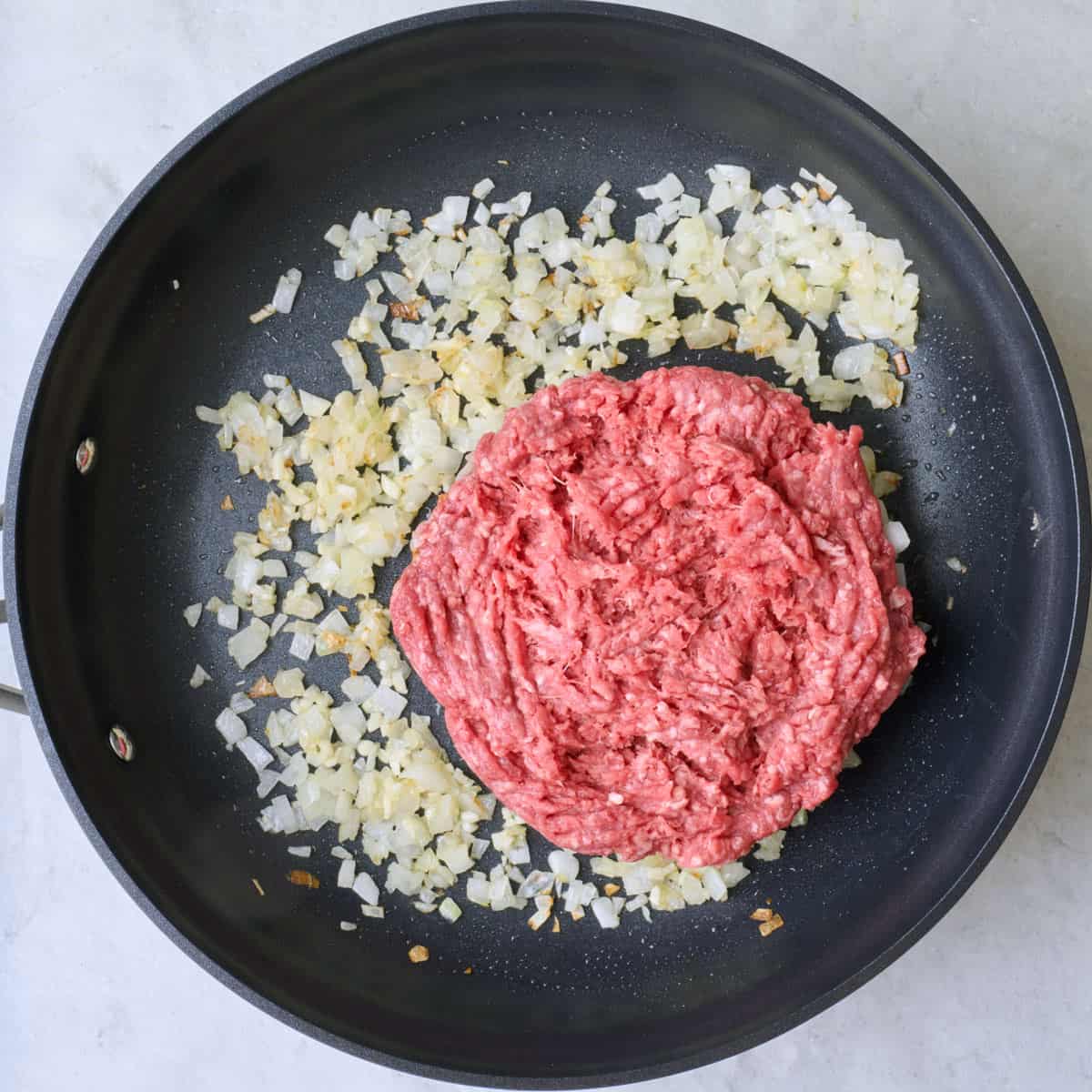 Onion and garlic in an oiled skillet after cooking with ground beef added.