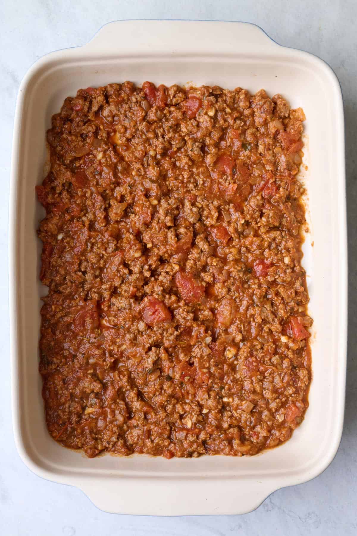 Half of ground beef marinara sauce spread into a baking dish.