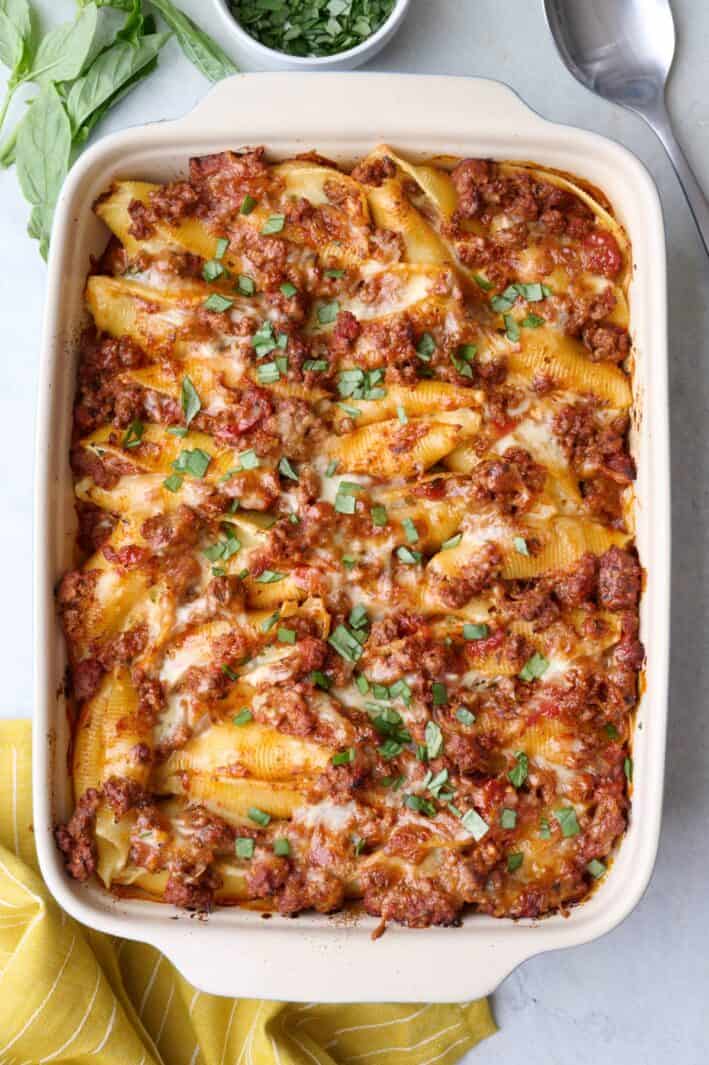 Beef stuffed shells in baking dish garnished with fresh chopped basil with serving spoon nearby.