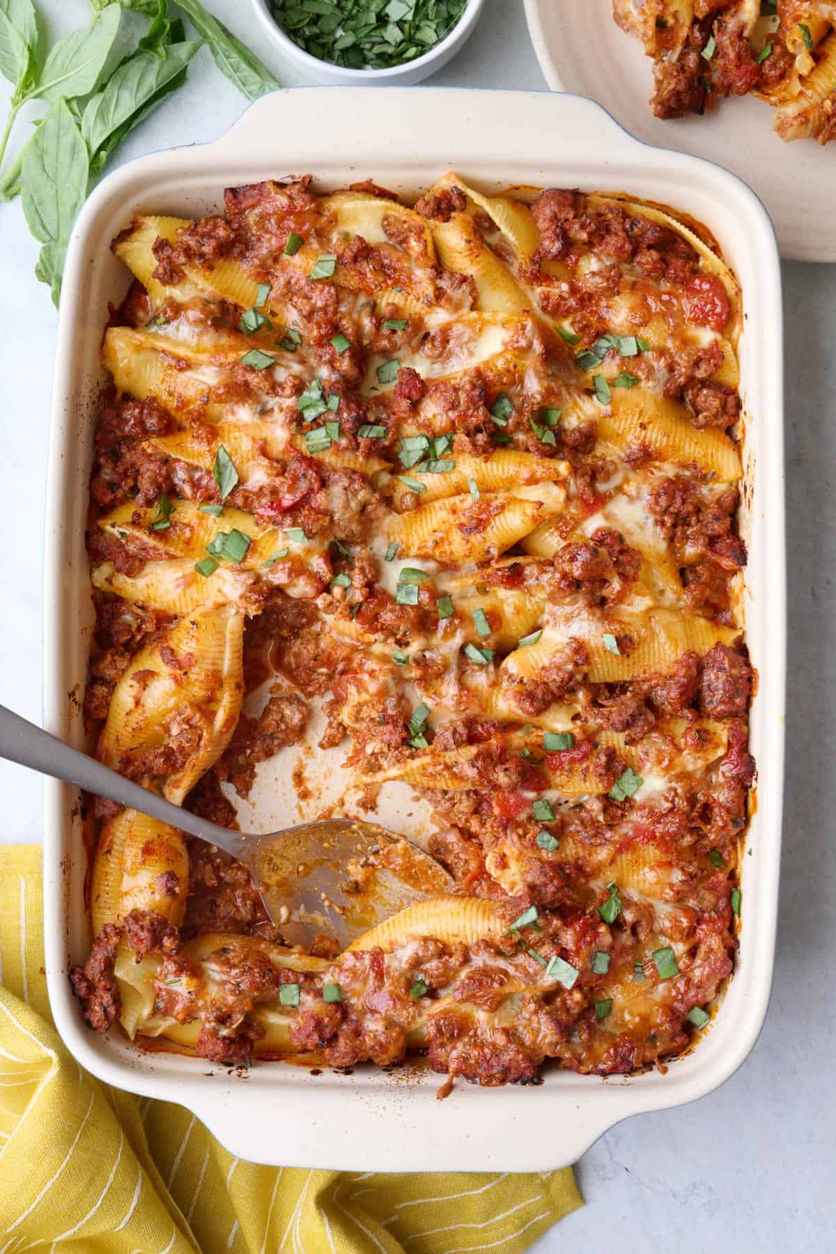 Beef stuffed shells in baking dish garnished with fresh chopped basil with serving spoon nearby.