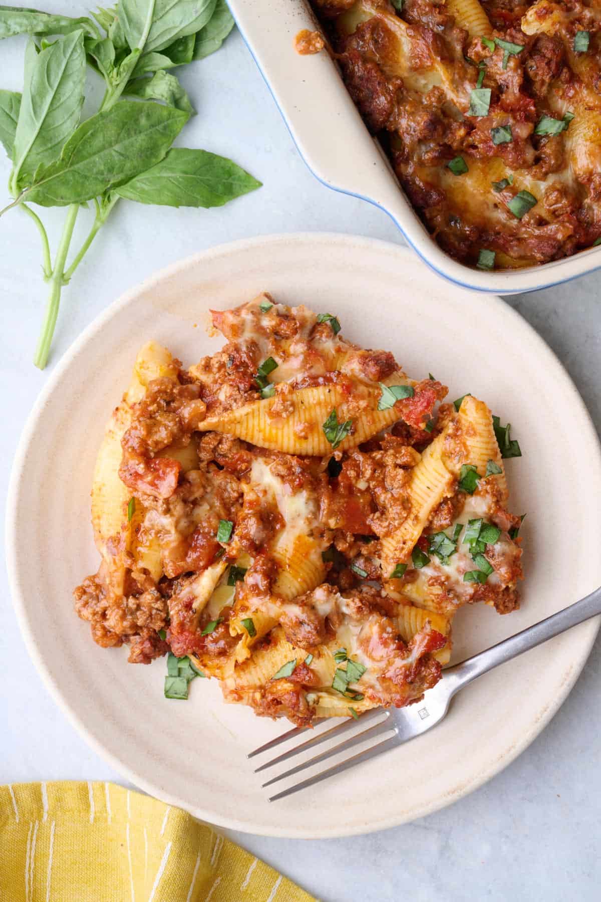 Serving of cheesy beef stuffed shells on a plate with baking dish nearby.