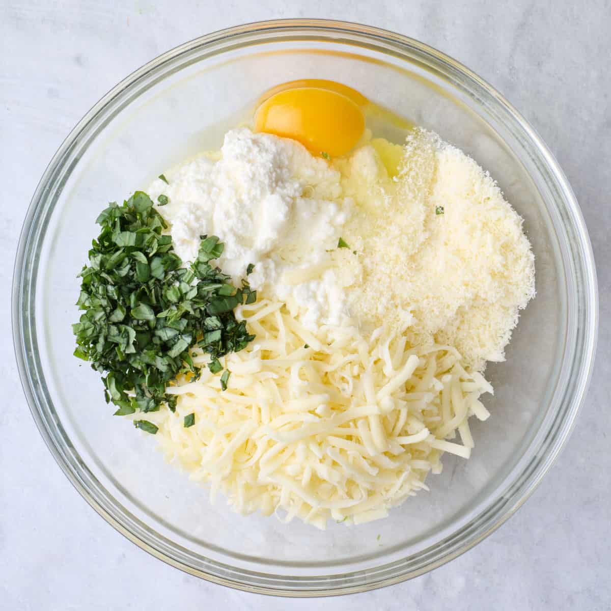 Ricotta, mozzarella, parmesan, basil and egg in a bowl.