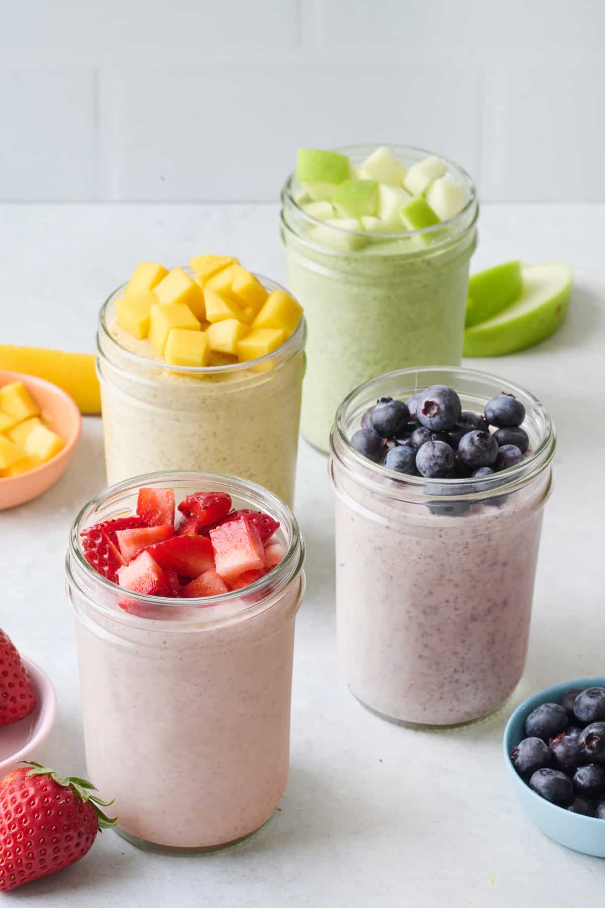 Blended overnight oat recipe made into four different flavors using fruit: strawberries, blueberries, mango, apples.