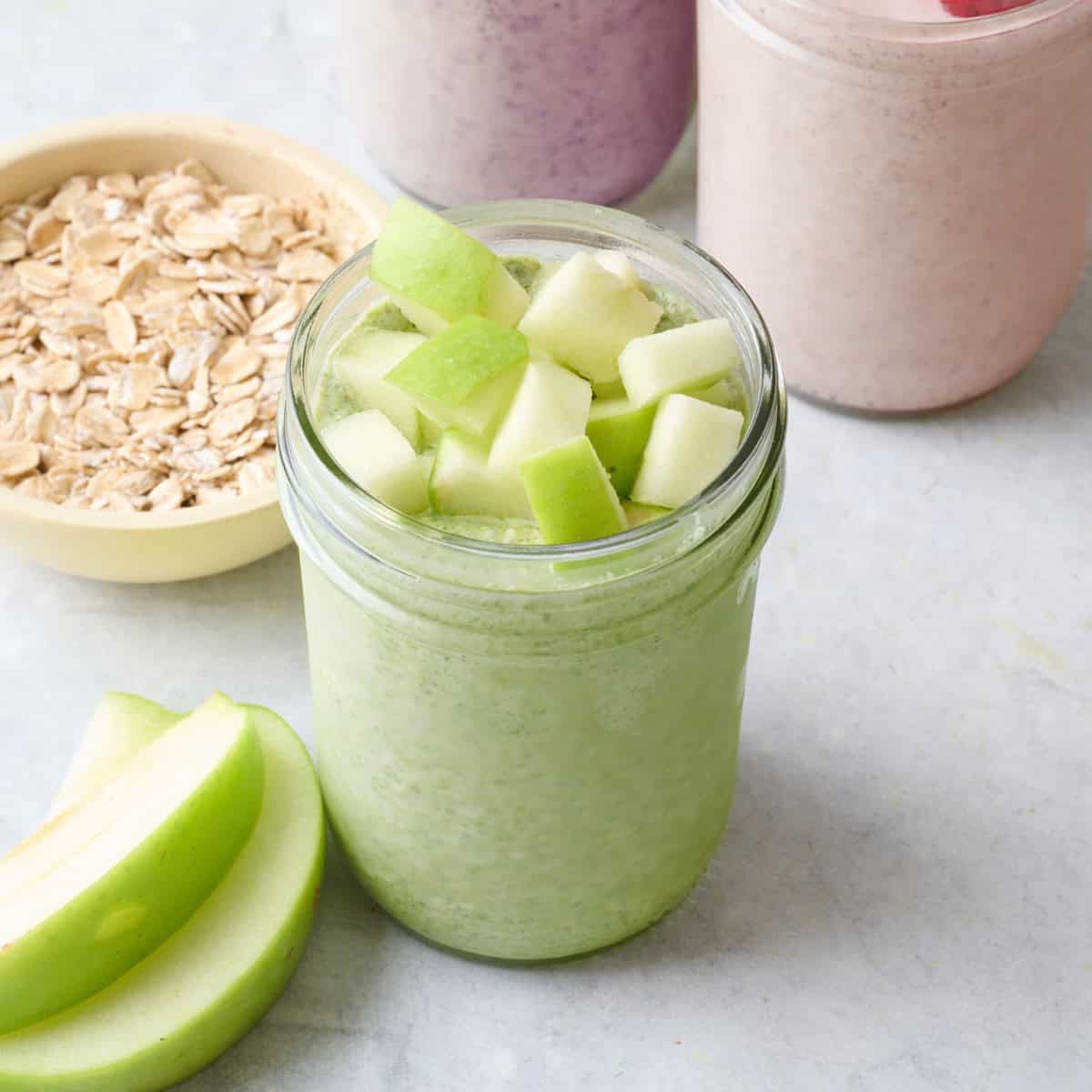 Spinach apple blended overnight oats in a small jar topped with fresh chopped apples.