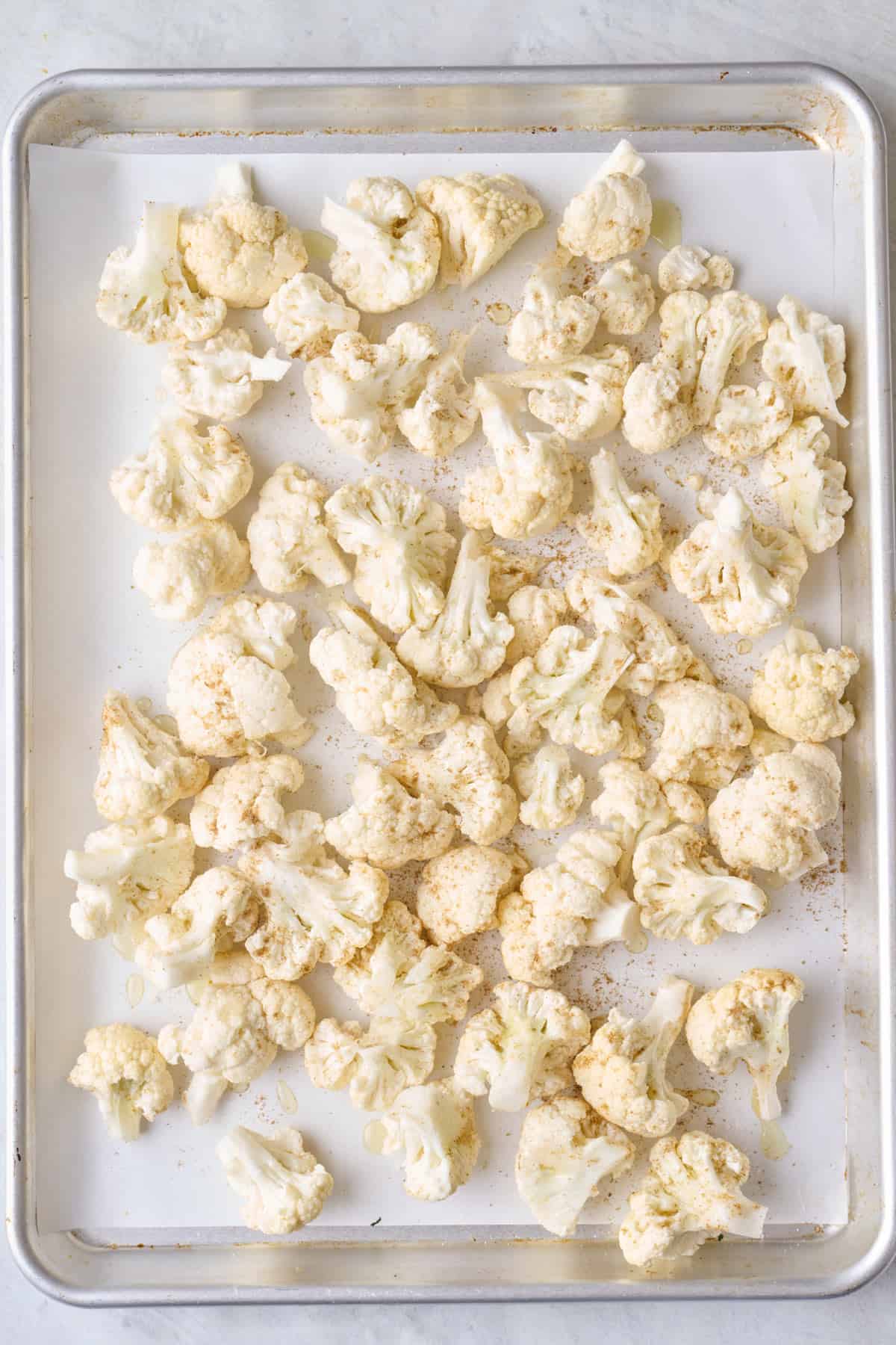 Seasoned and oiled cauliflower florets on a baking sheet before baking.