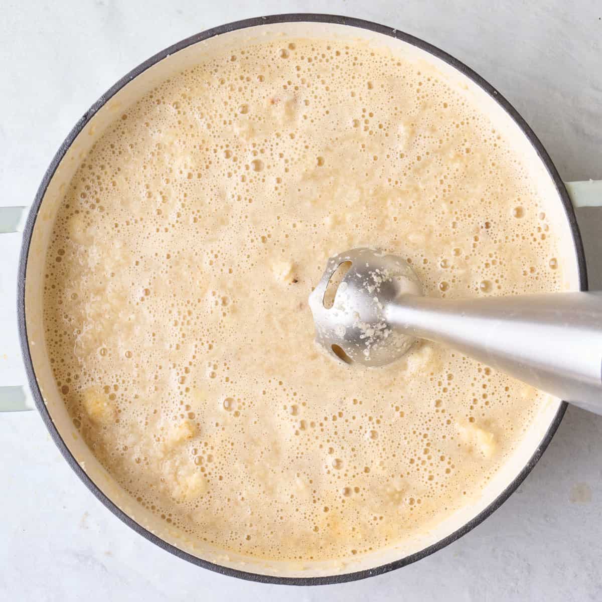 Immersion blended dipped into partially blended soup in a pot.