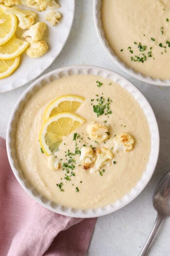 Two bowls of homemade creamy cauliflower soup garnished with extra roasted cauliflower florets and lemon slices.