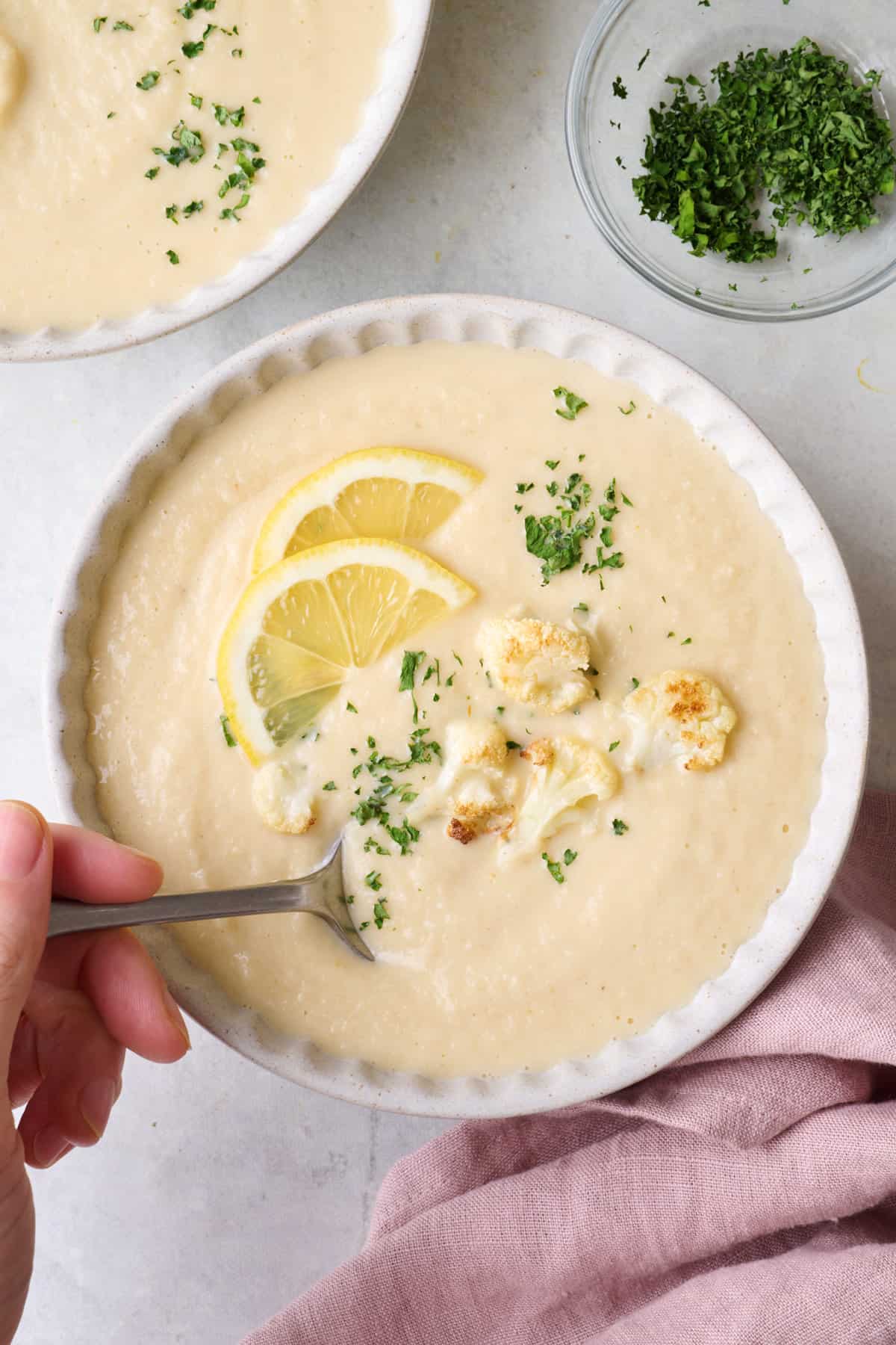 Spoon dipped into a bowl of creamy roasted cauliflower soup.