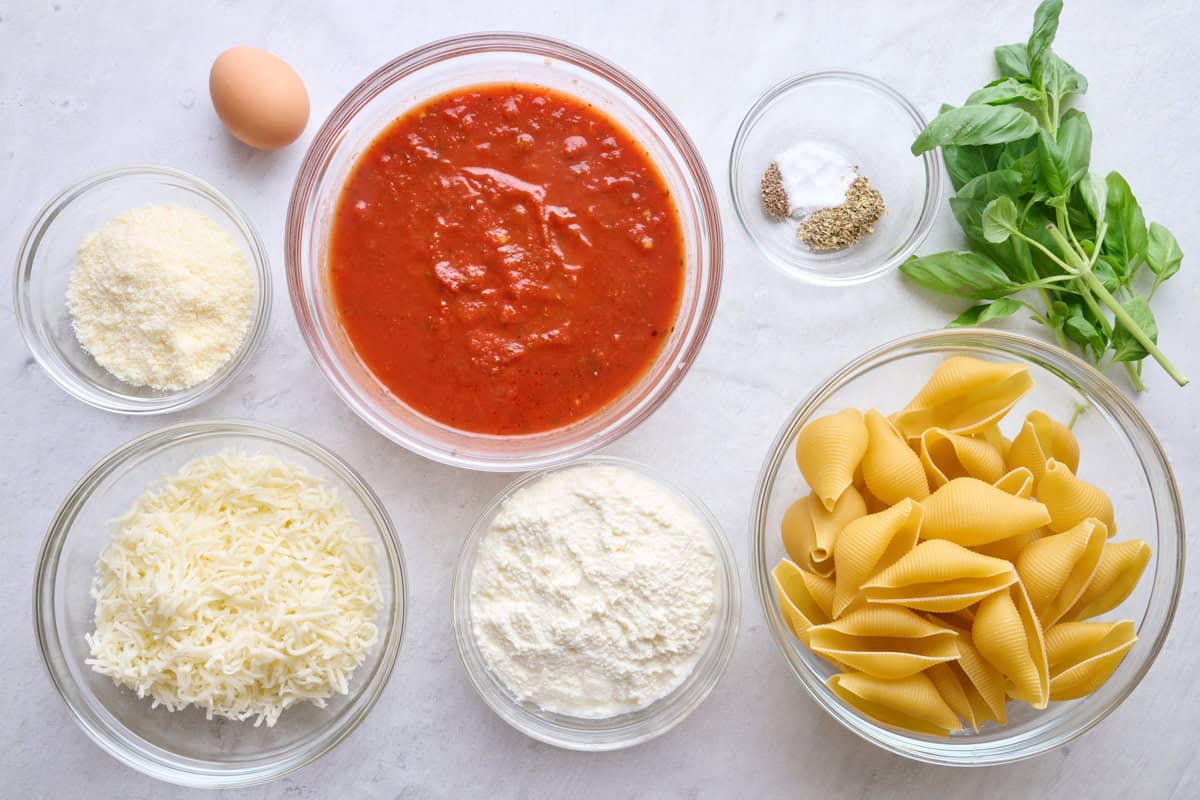 Ingredients for recipe: grated parmesan cheese, shredded mozzarella, ricotta, marinara sauce, egg, seasonings, fresh basil and uncooked jumbo pasta shells.