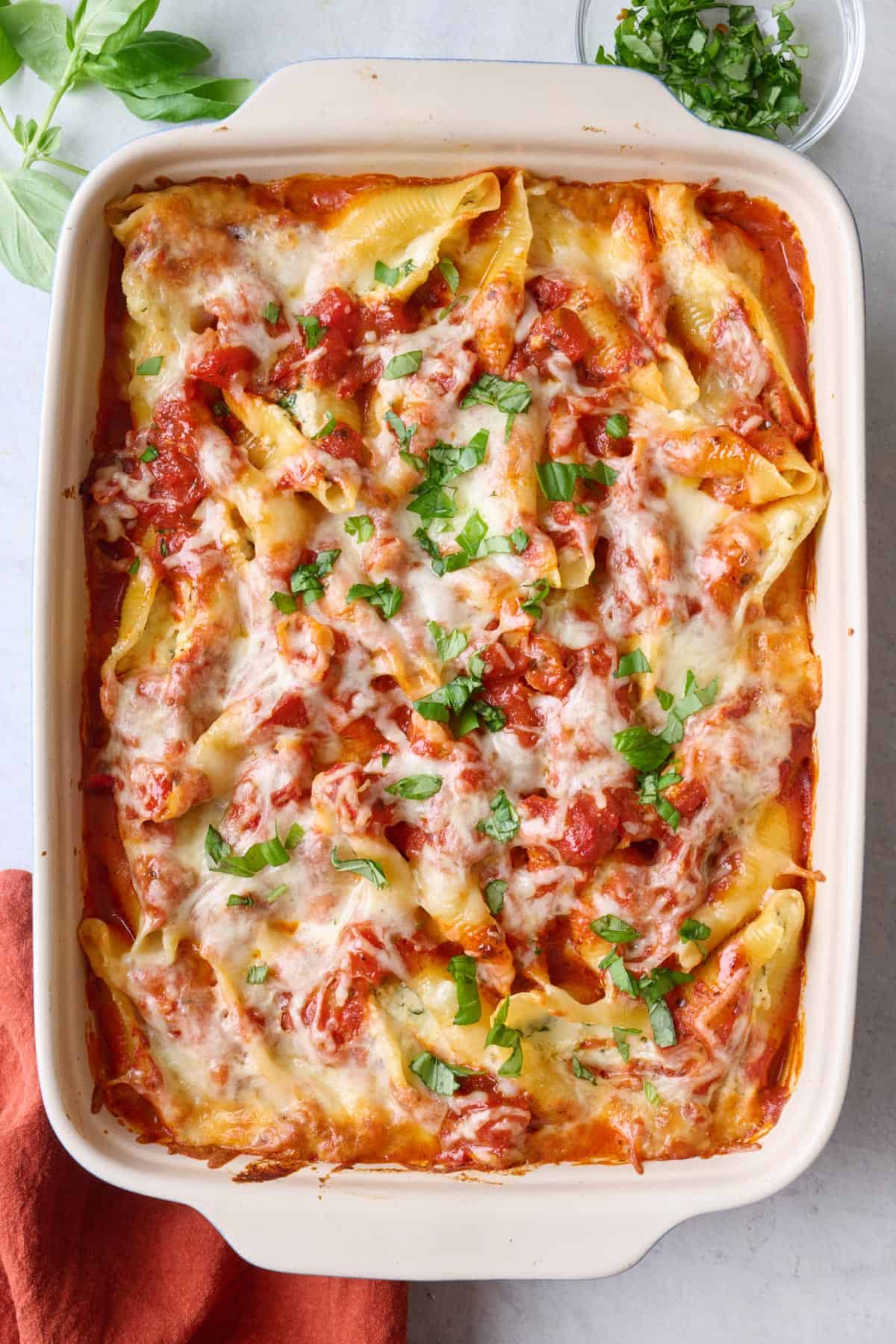 Cheese stuffed shells in baking dish garnished with fresh basil with serving spoon nearby.