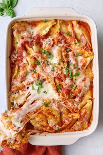 Baking dish of cheese stuffed shells recipe with a bite being removed showing cheesy pull.