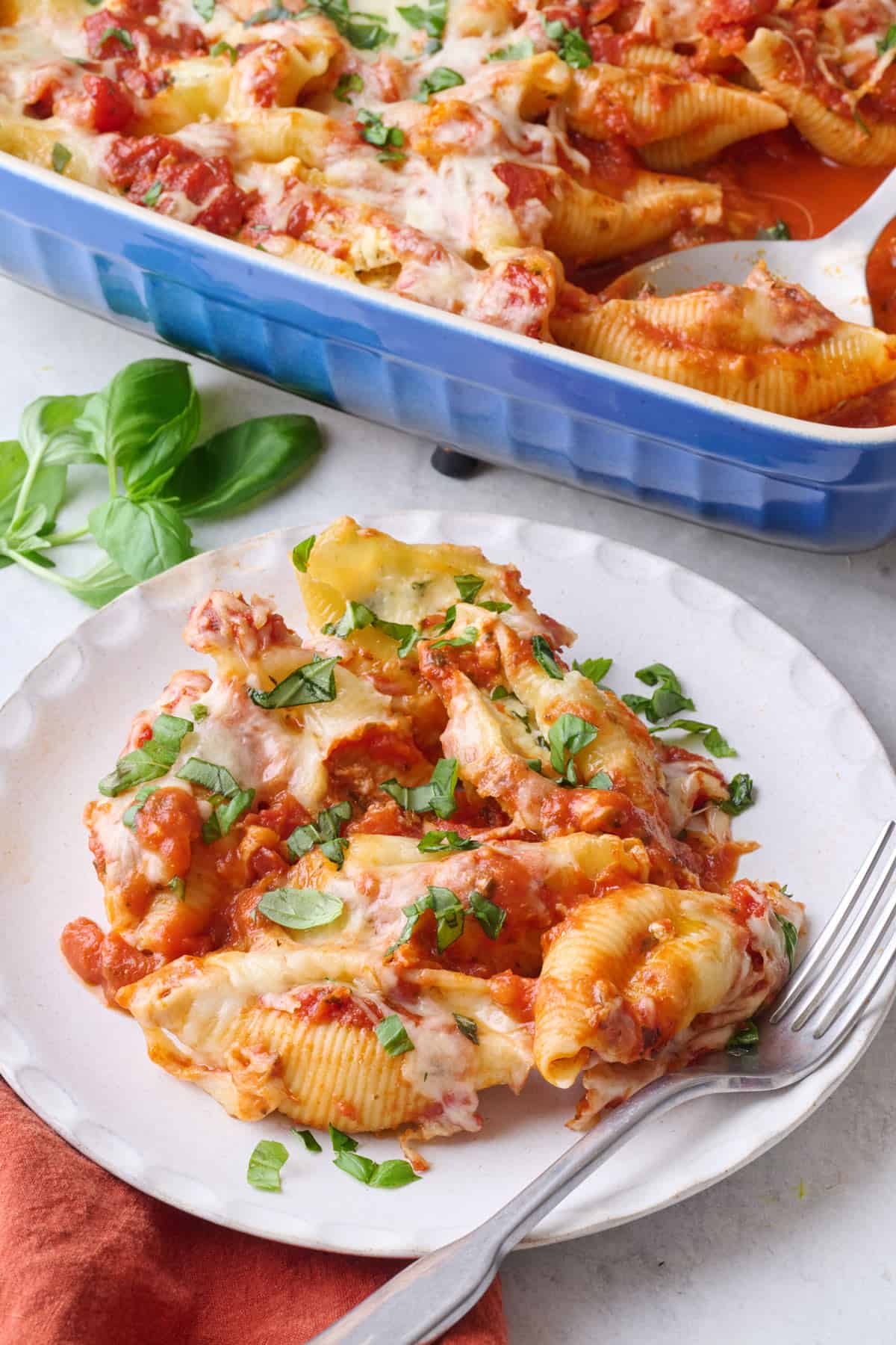 Serving of stuffed cheese shells on plate with baking dish nearby.