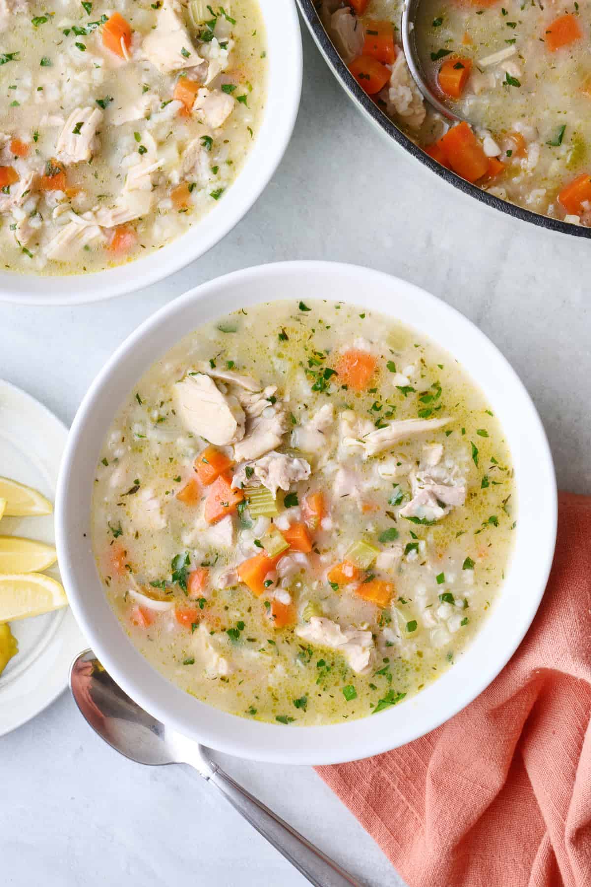 Two bowls of homemade chicken lemon rice soup with pot nearby.