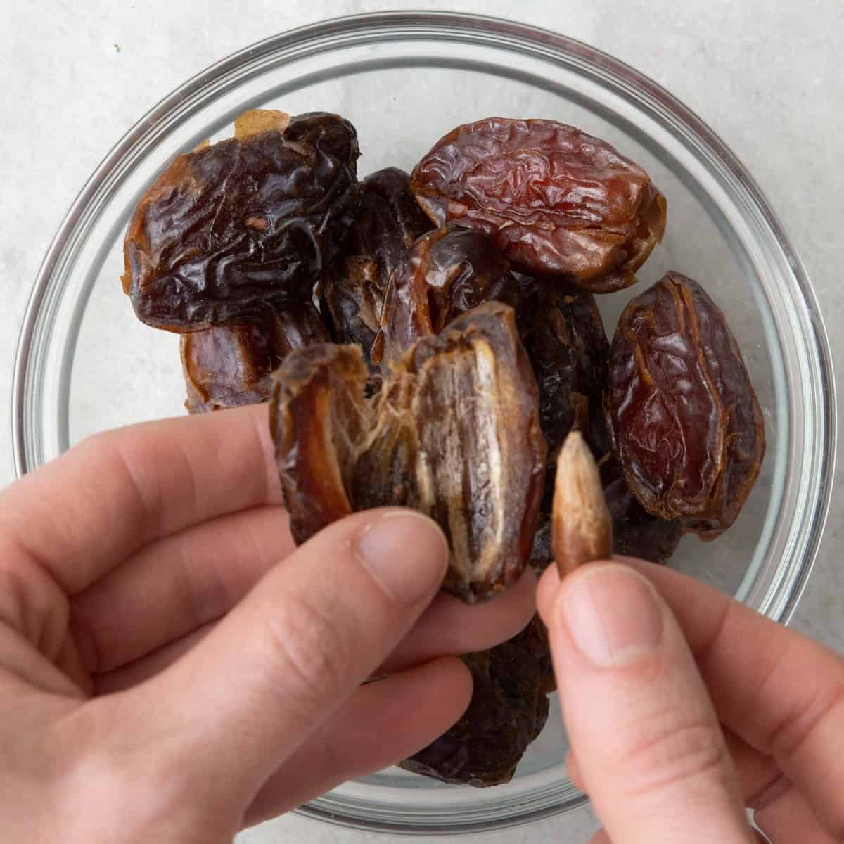 Fingers holding date and removing pit over bowl of more dates.