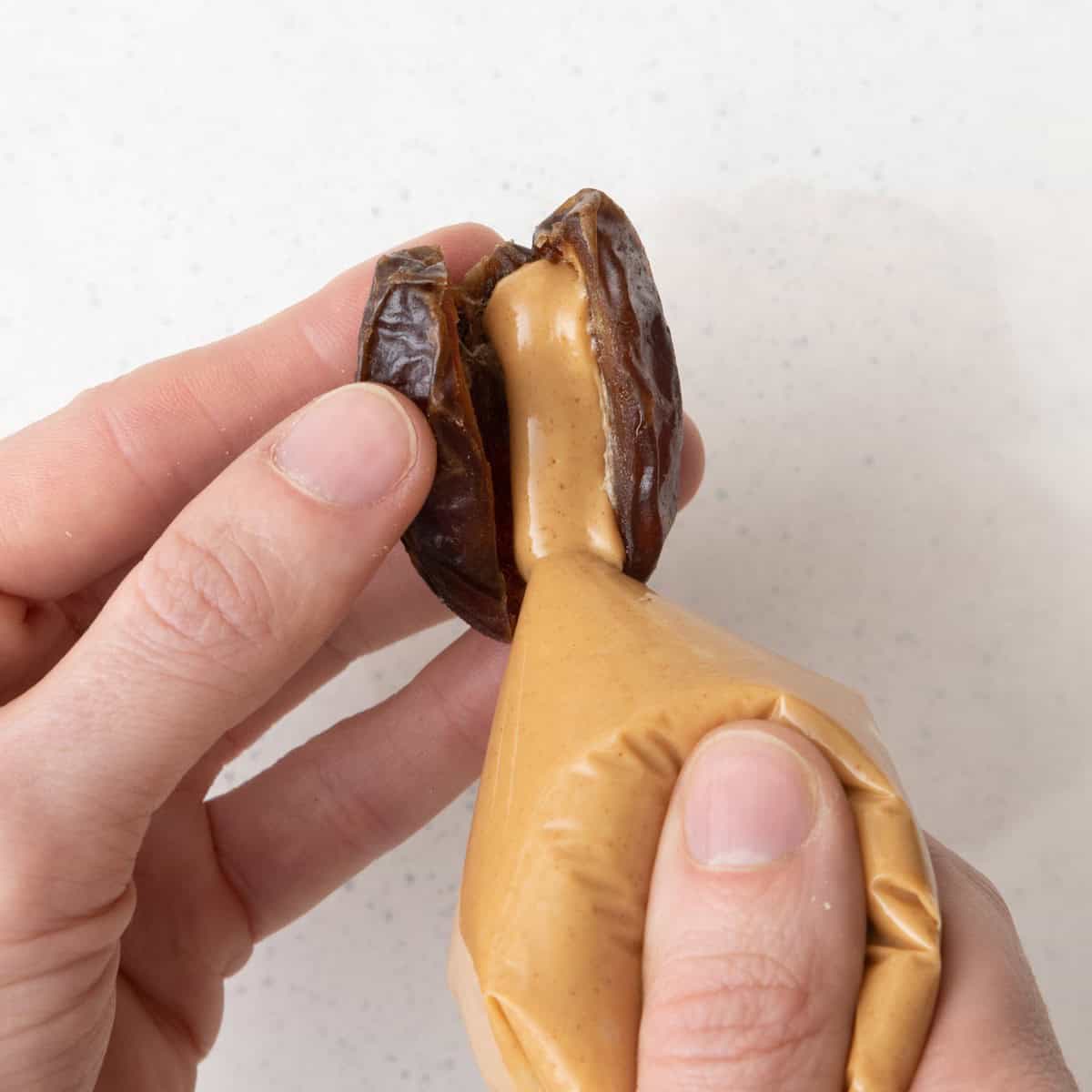 Hand holding split date and squeezing peanut butter inside form a bag.