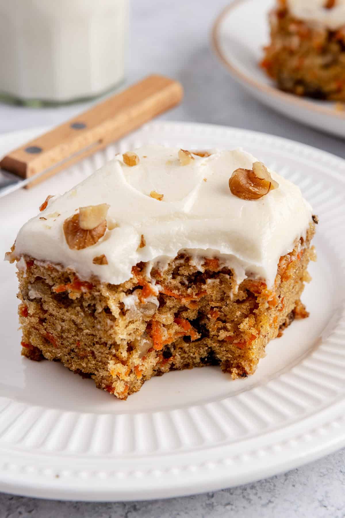 Slice of carrot cake on a plate with a bite removed.
