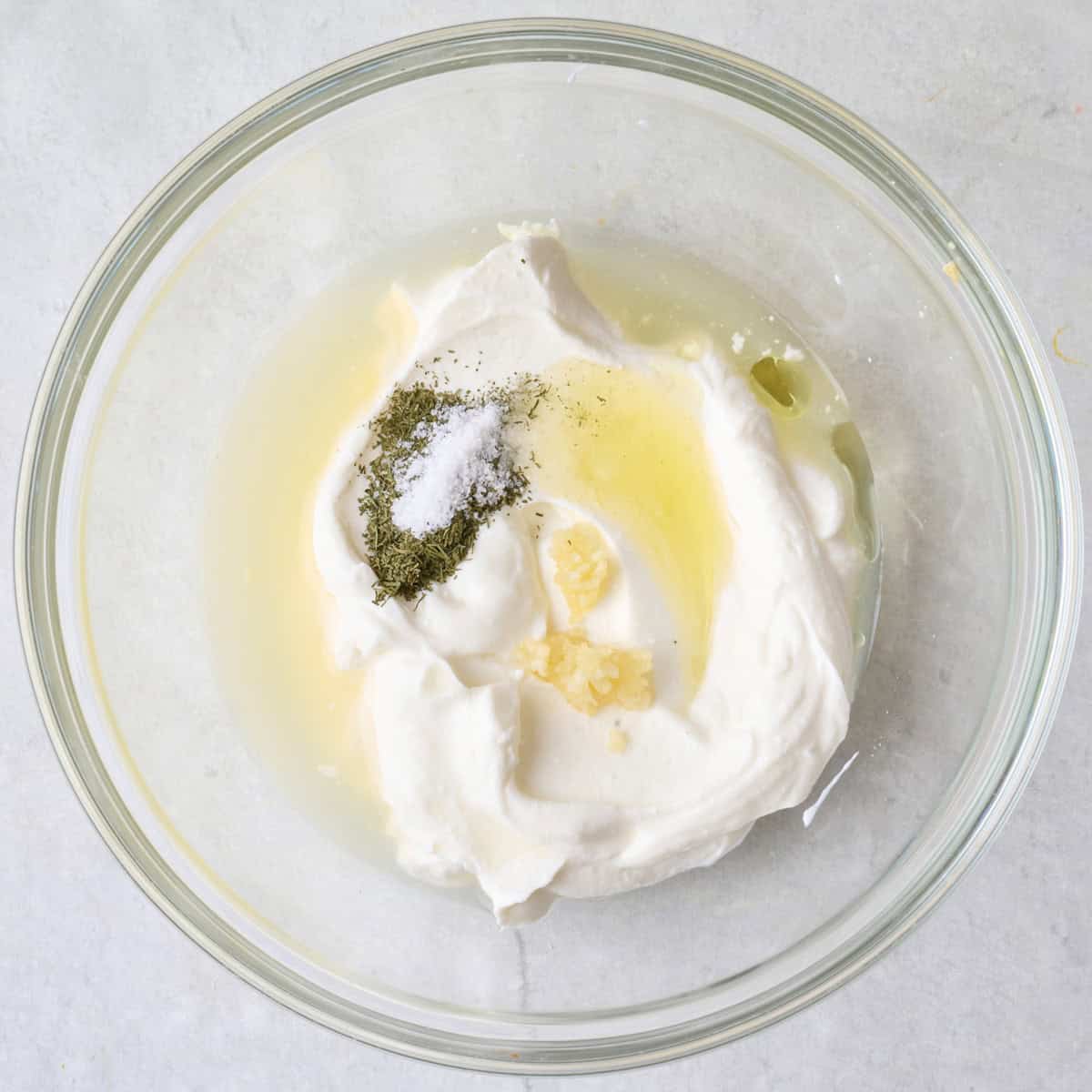 Greek yogurt, olive oil, lemon juice, dill powder and salt in a bowl before mixing.