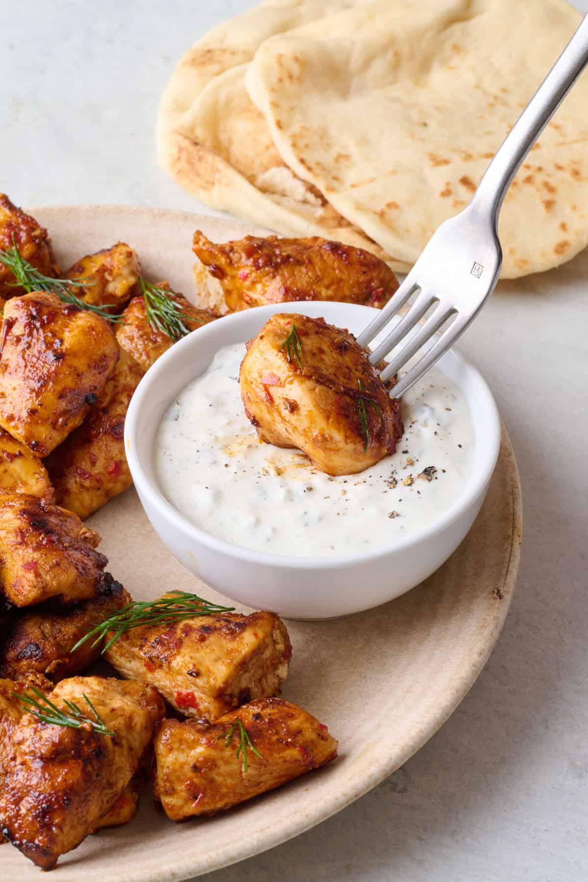 Chicken bites being dipped into Greek yogurt sauce with a fork.