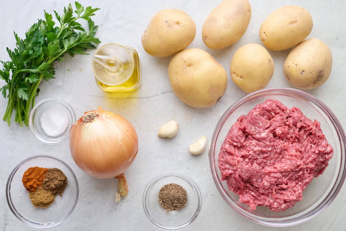 Ingredients for recipe before prepping: fresh parsley, salt, paprika, 7 spice, ground cumin, onion, oil, potatoes, garlic, pepper, ground beef.