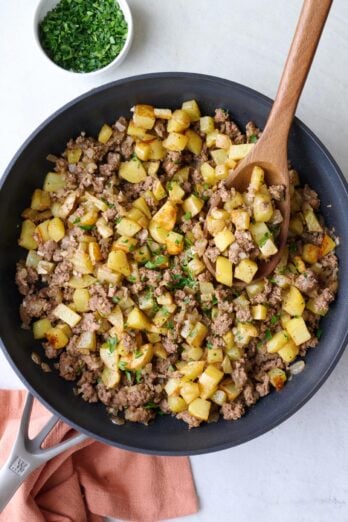 Ground beef and potatoes in the skillet garnished with parsley and a serving spoon dipped inside.