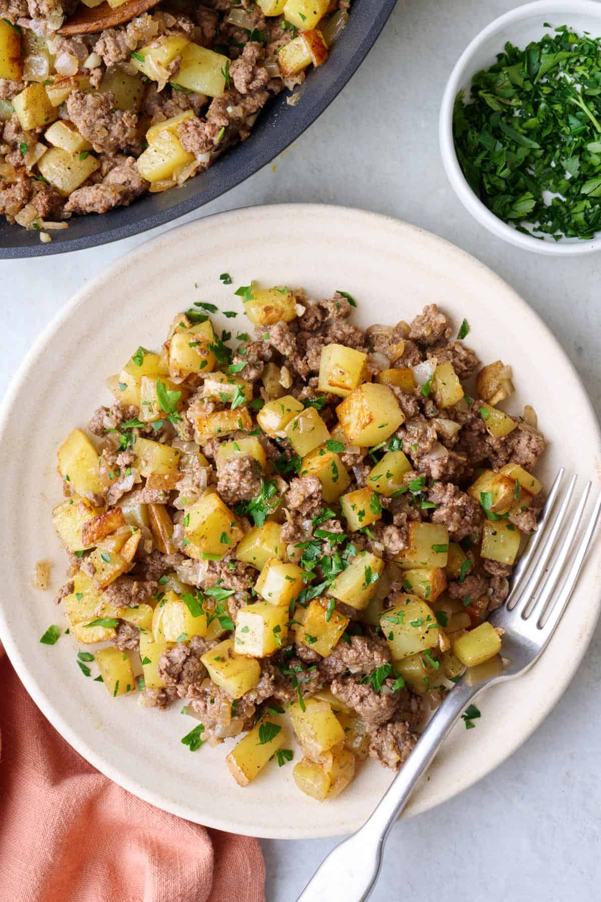 Serving of ground beef and potatoes on a plate garnished with fresh parsley.